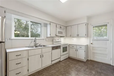 a kitchen with white cabinets appliances a sink and a window