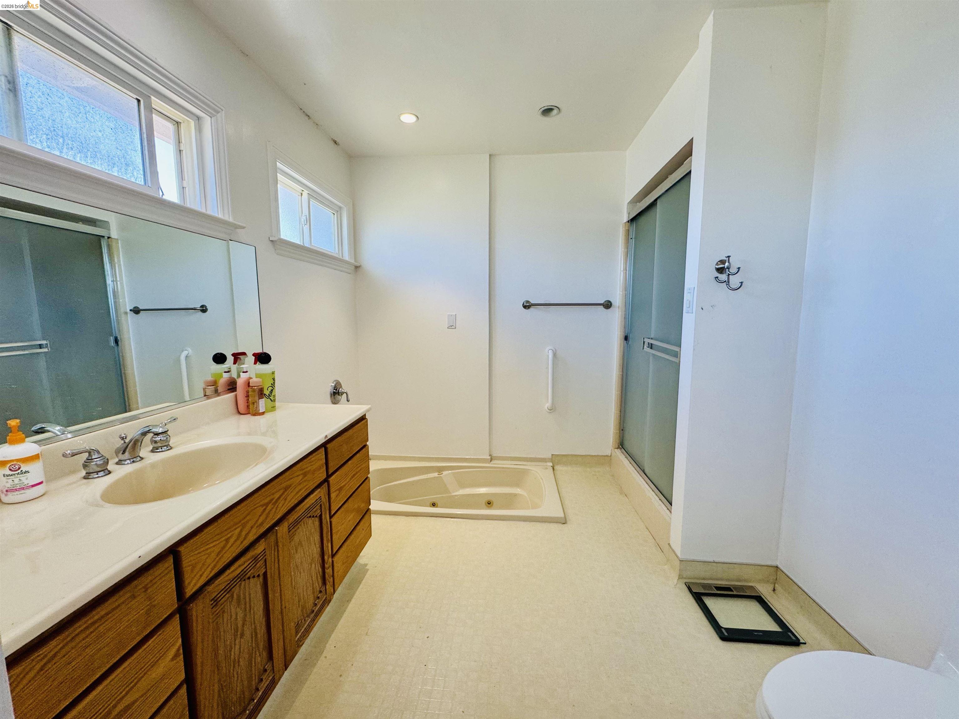 64 Washington Street Novato, CA 94947 - Photo 14 of 21 Bathroom featuring a built-in jetted tub, a separate shower with sliding frosted glass doors, and a wood-finish vanity with an integrated sink and light-toned countertop