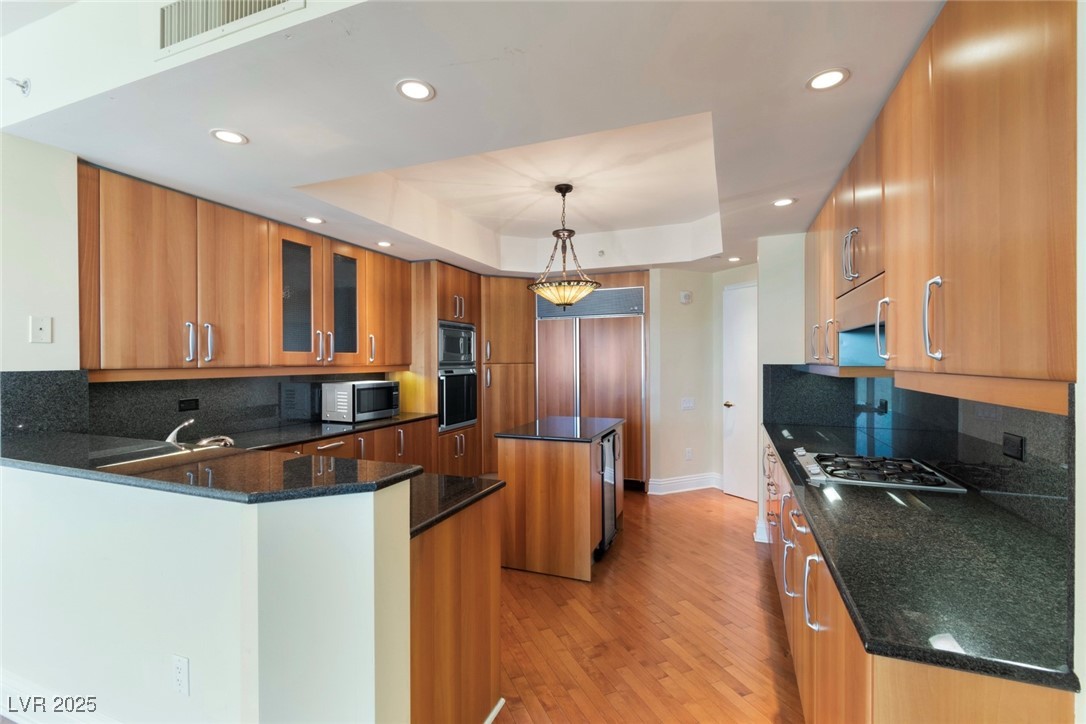 2857 Paradise Road, Unit 802 Las Vegas, NV 89109 - Photo 8 of 36 Kitchen featuring appliances with stainless steel finishes, brown cabinets, a tray ceiling, recessed lighting, and a center island