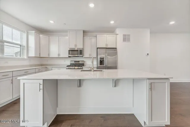 a kitchen with stainless steel appliances granite countertop a sink a stove a refrigerator and white cabinets