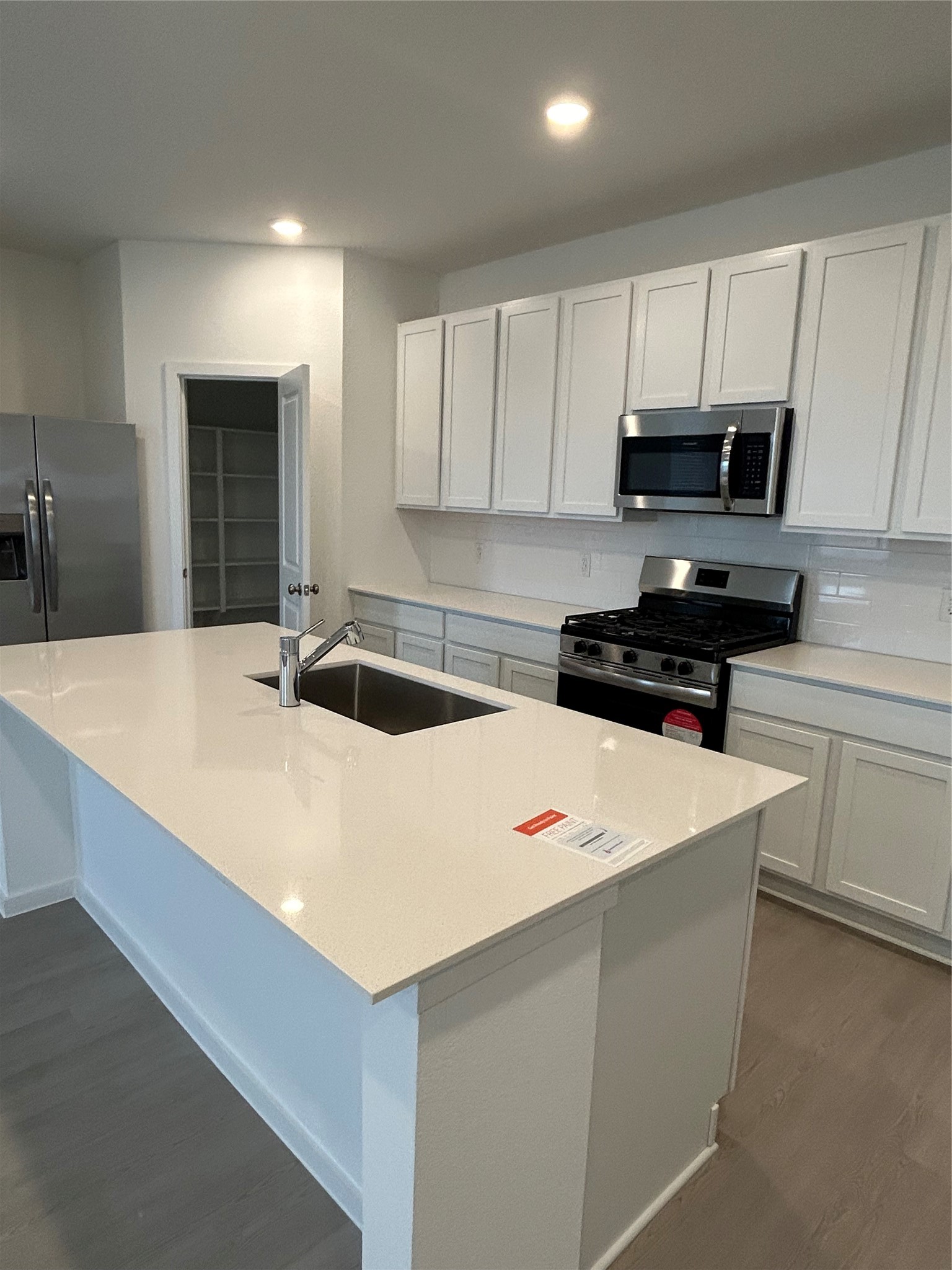 26419 Virginia Wild Rye Lane Katy, TX 77493 - Photo 12 of 31 This modern kitchen features sleek white cabinetry, stainless steel appliances, and a spacious island with a sink. It includes a gas stove, built-in microwave, and a large refrigerator. The open layout is complemented by a pantry for additional storage.