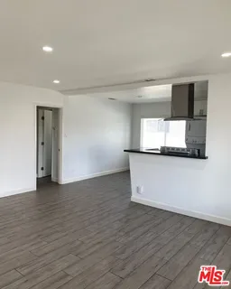 a view of empty room with wooden floor and kitchen