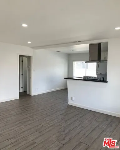 a view of empty room with wooden floor and kitchen