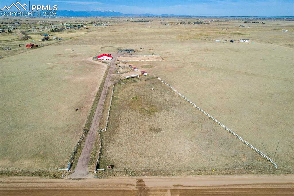 7880 J D Johnson Road Peyton, CO 80831 - Photo 26 of 50 Expansive rural property featuring a main building with a red roof, multiple outbuildings, and a white perimeter fence