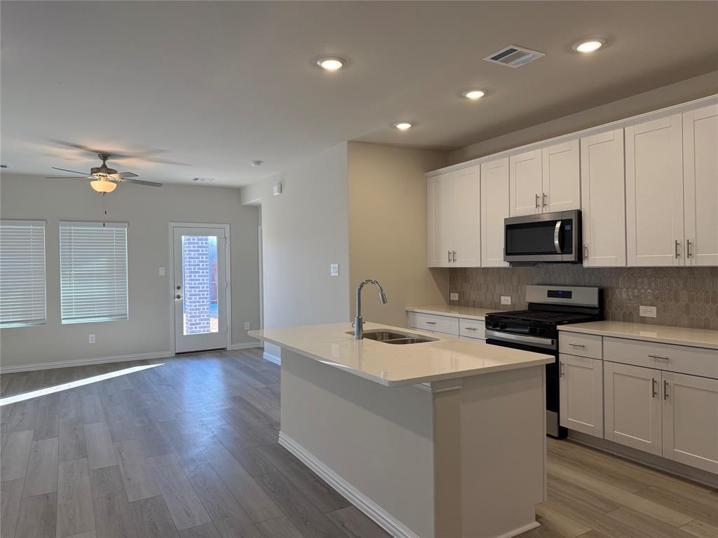 1736 Arches Road Anna, TX 75409 - Photo 17 of 18 Kitchen featuring stainless steel appliances, a kitchen island with sink, white cabinetry, light wood-style flooring, and open floor plan