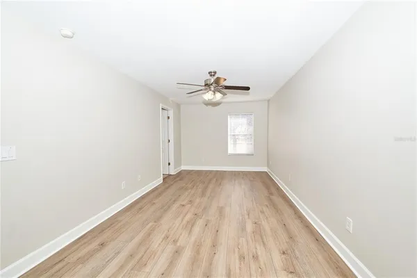 an empty room with wooden floor ceiling fan and window