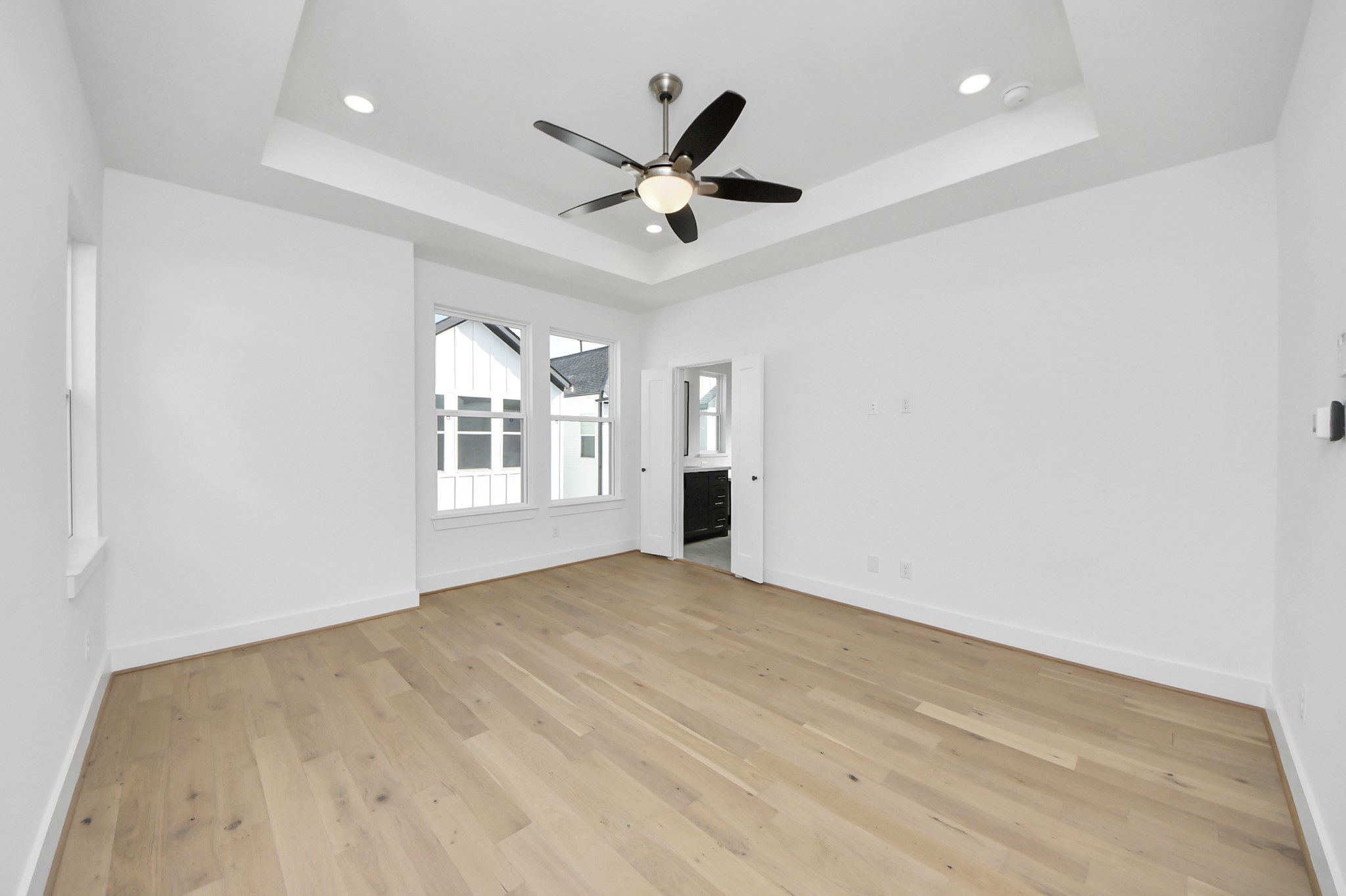 723 Marcella Street, Unit D Houston, TX 77091 - Photo 13 of 22 This bright, spacious room features light hardwood flooring, a tray ceiling with recessed lighting, and a ceiling fan. Large windows provide ample natural light, and the room offers access to an adjoining space or bathroom through a doorway.