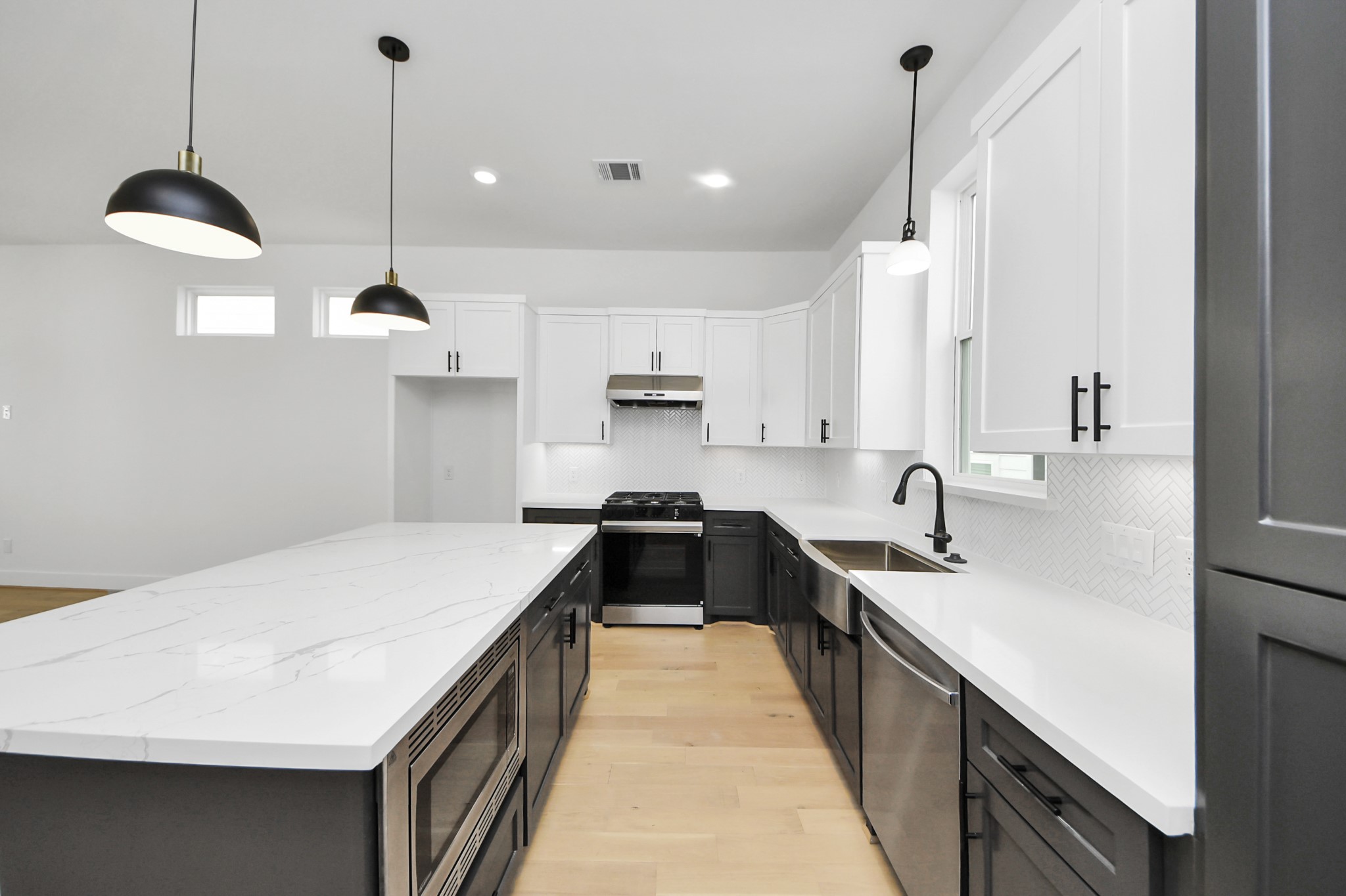 723 Marcella Street, Unit D Houston, TX 77091 - Photo 9 of 22 This modern kitchen features sleek white cabinetry with black accents, a spacious central island with a marble-like countertop, and stainless steel appliances. The room is well-lit with pendant lights and natural light from small windows, creating a bright and inviting space.