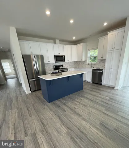 a kitchen with stainless steel appliances wooden floors wooden cabinets a refrigerator and microwave