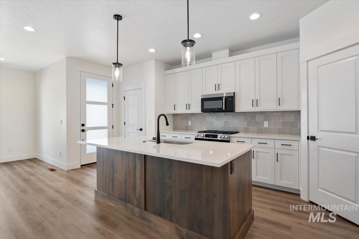 768 South Calhoun Lane Star, ID 83669 - Photo 11 of 36 Modern kitchen featuring a central island with white countertop, white cabinetry with black hardware, stainless steel appliances, and wood-finish flooring