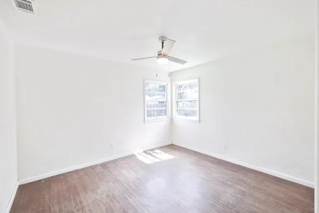an empty room with wooden floor chandelier fan and windows