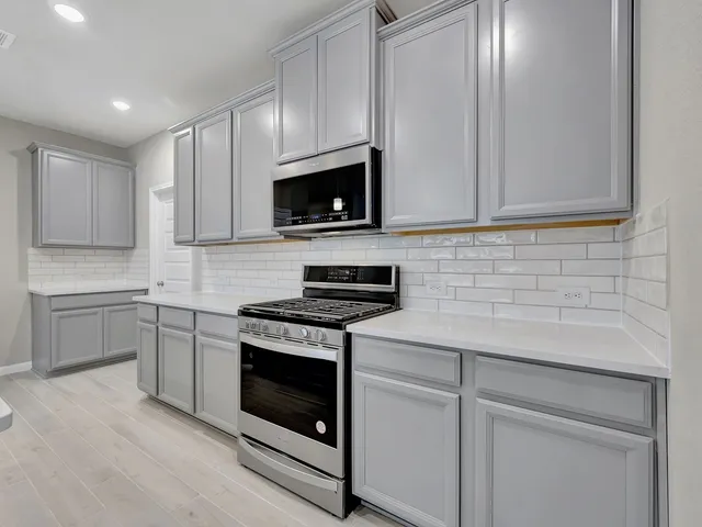 a kitchen with stainless steel appliances granite countertop grey cabinets a stove a sink and dishwasher