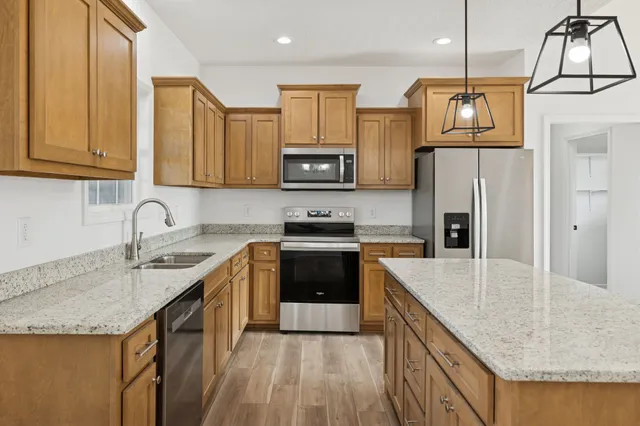 a large kitchen with kitchen island a stove a sink dishwasher a refrigerator white cabinets and wooden floor next to a window