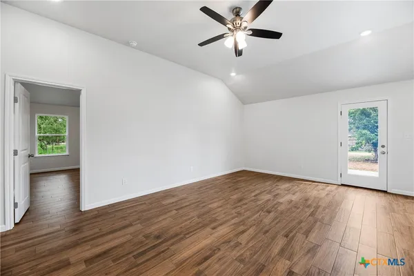 an empty room with wooden floor chandelier fan and windows