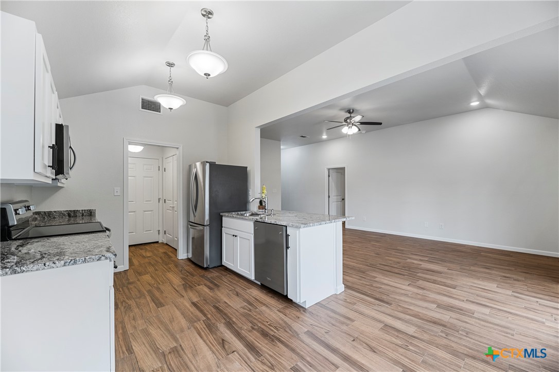 230 Plum Street Luling, TX 78648 - Photo 20 of 33 a large kitchen with kitchen island a stove a sink dishwasher a refrigerator and a fireplace with wooden floor