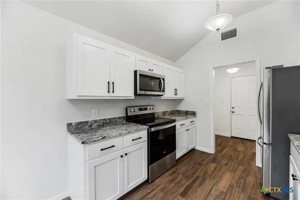 a kitchen with granite countertop a refrigerator stove top oven and sink