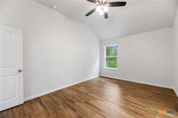 an empty room with wooden floor chandelier fan and windows