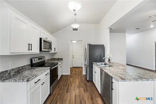 a kitchen with stainless steel appliances granite countertop a stove top oven a sink dishwasher and a refrigerator with wooden floor