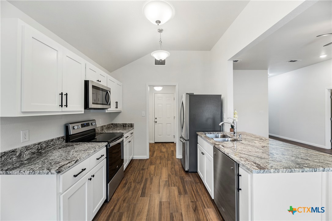 230 Plum Street Luling, TX 78648 - Photo 5 of 33 a kitchen with stainless steel appliances granite countertop a stove top oven a sink dishwasher and a refrigerator with wooden floor