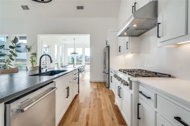 a kitchen with granite countertop a stove a sink dishwasher and white cabinets with wooden floor