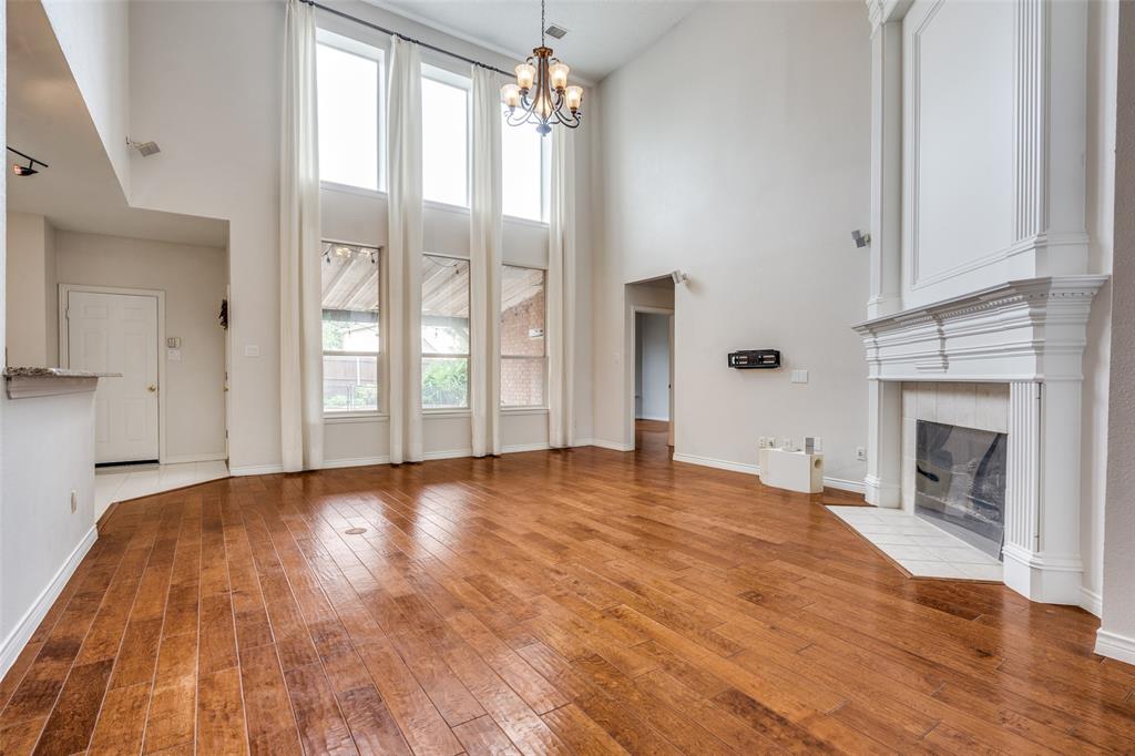 3421 Neiman Road Plano, TX 75025 - Photo 7 of 40 Unfurnished living room with a towering ceiling, healthy amount of natural light, hardwood / wood-style flooring, a high end fireplace, and a chandelier
