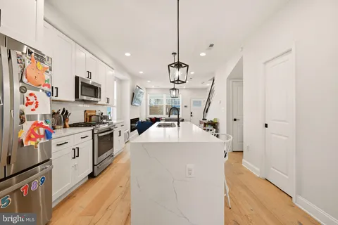 a white kitchen with stainless steel appliances granite countertop a sink dishwasher a refrigerator and a stove with wooden floor