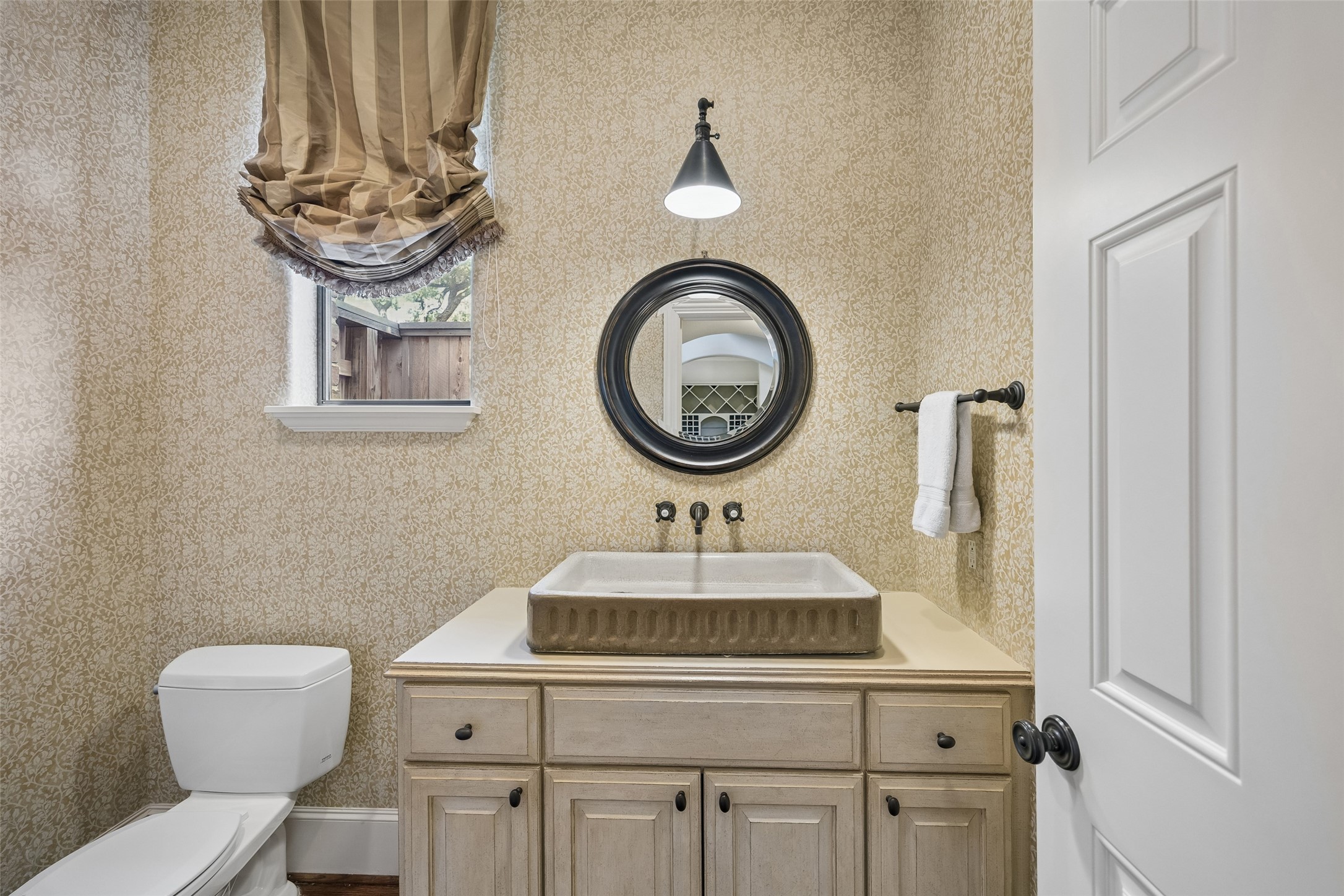 6261 Burgoyne Road Houston, TX 77057 - Photo 23 of 40 Charming powder room featuring a vessel sink atop a wooden vanity, complemented by elegant wallpaper and a round mirror for a touch of sophistication.