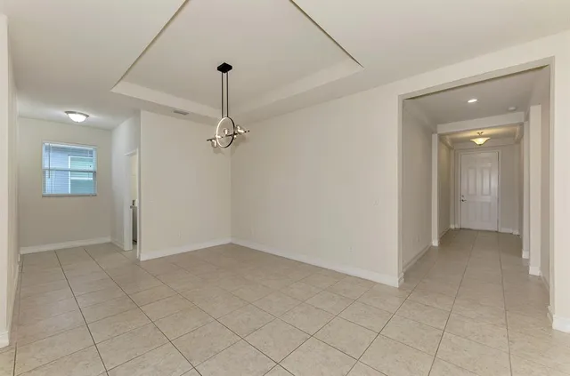 an empty room with chandelier fan and kitchen view