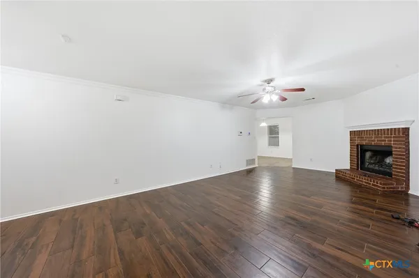 an empty room with wooden floor fireplace and chandelier fan