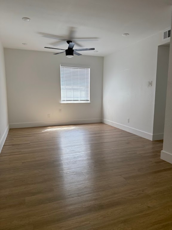 an empty room with wooden floor chandelier fan and windows