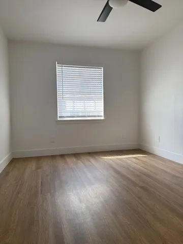 an empty room with wooden floor fan and windows