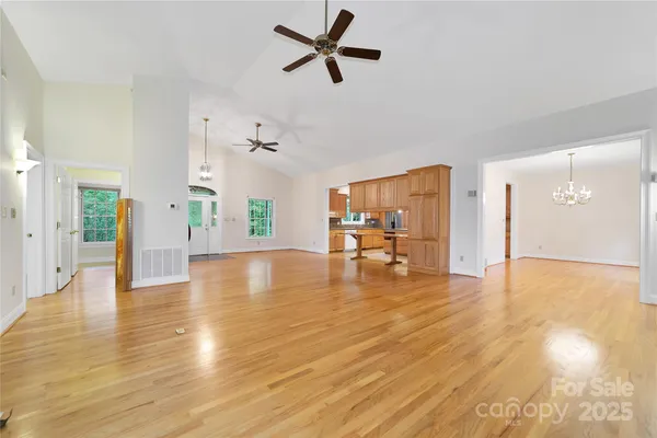 a view of an empty room and kitchen with wooden floor