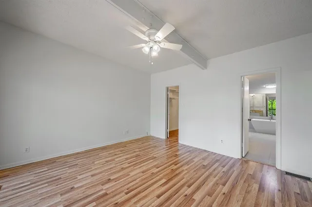 a view of an empty room with wooden floor and a ceiling fan