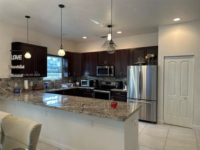 a kitchen with stainless steel appliances granite countertop a refrigerator a stove a sink and a microwave