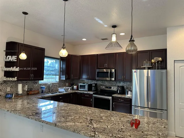 a kitchen with stainless steel appliances granite countertop a refrigerator a stove a sink dishwasher a refrigerator and a microwave with wooden floor