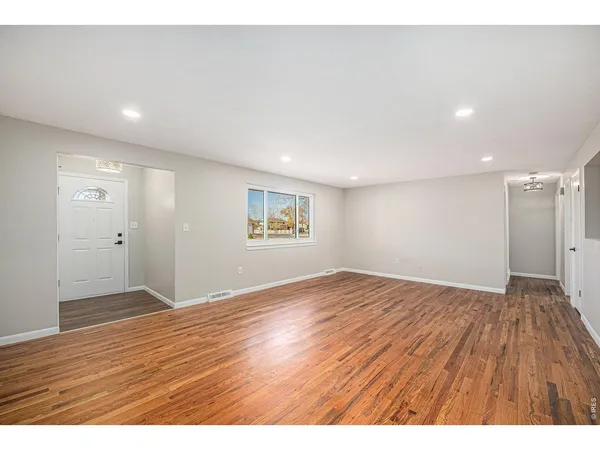 a view of an empty room with wooden floor and a window