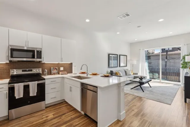 a open kitchen with stainless steel appliances granite countertop a stove top oven a sink dishwasher a dining table and chairs with wooden floor