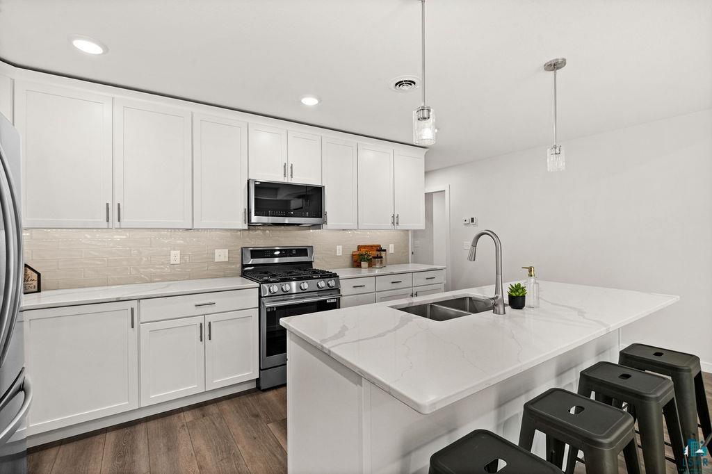 3971 Haines Road Hermantown, MN 55811 - Photo 16 of 34 Modern kitchen featuring white shaker cabinetry, stainless steel appliances, a center island with a double basin sink, light-colored countertops, and wood-finish flooring