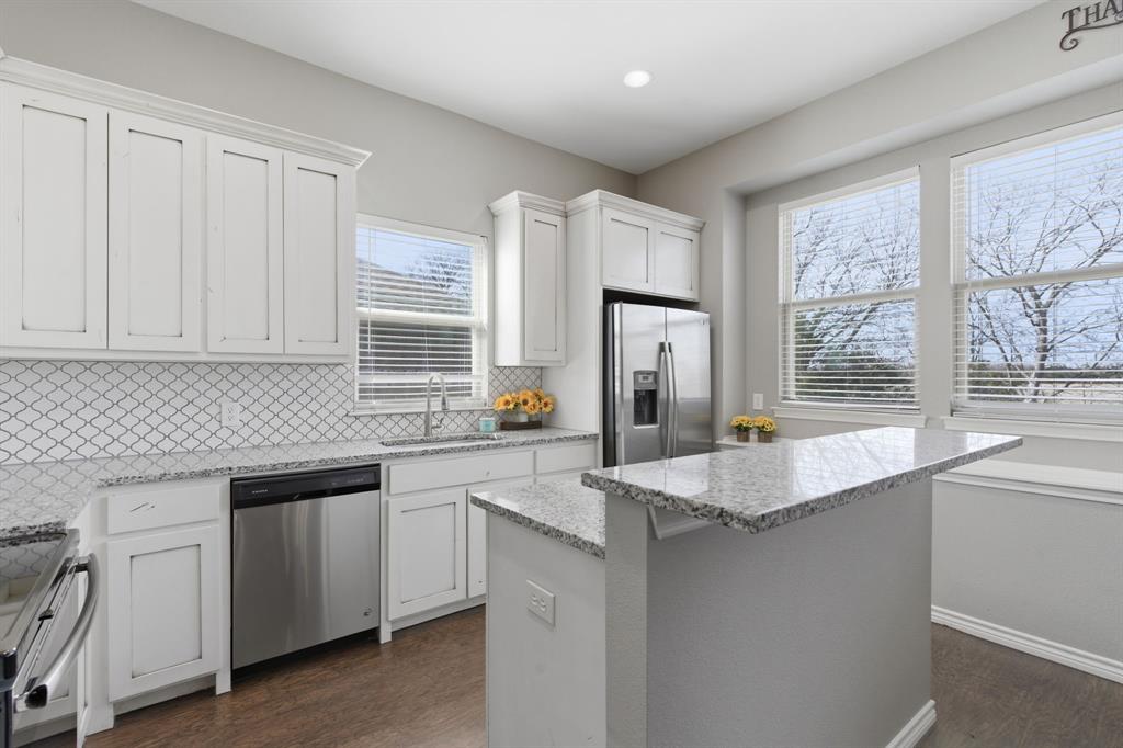 711 Hadley Lane Valley View, TX 76272 - Photo 12 of 40 Kitchen with white cabinetry, dark wood-type flooring, stainless steel appliances, tasteful backsplash, and a kitchen island