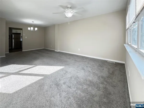 an empty room with chandelier fan and windows