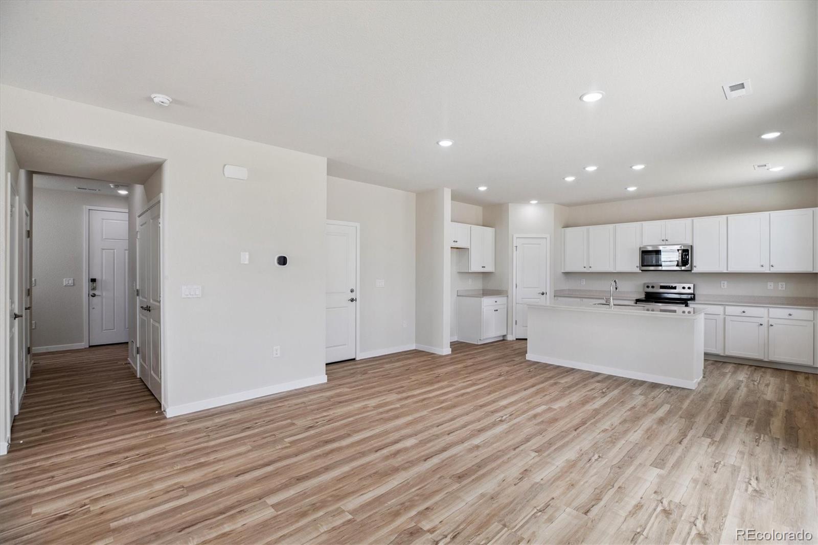 42591 Kinloch Trail Elizabeth, CO 80107 - Photo 6 of 21 a large white kitchen with kitchen island a sink dishwasher a refrigerator and white cabinets with wooden floor