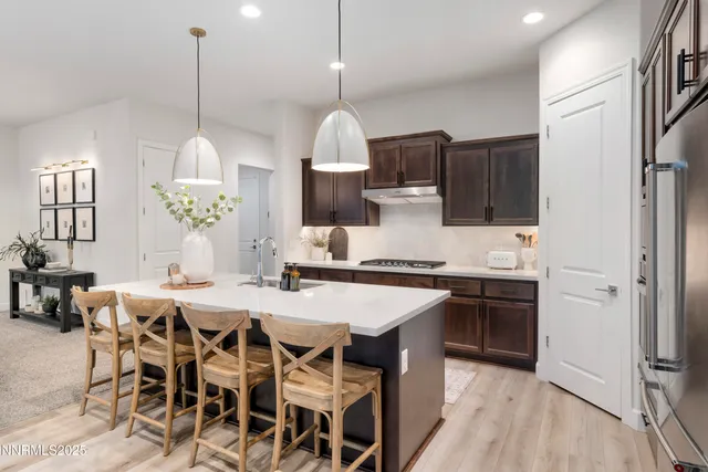 a kitchen with stainless steel appliances kitchen island granite countertop a stove a sink a oven a dining table and chairs with wooden floor