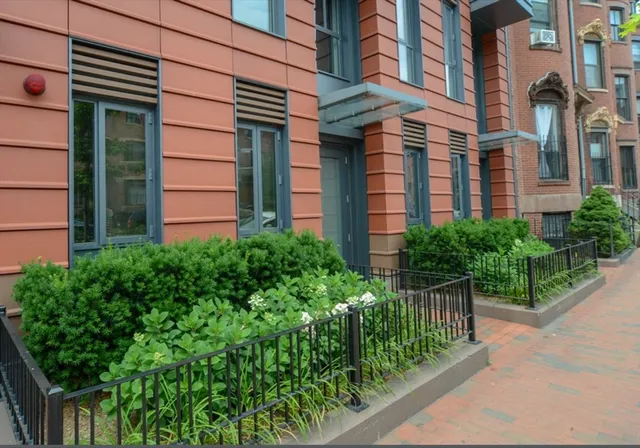 a view of a brick house with plants and a large tree