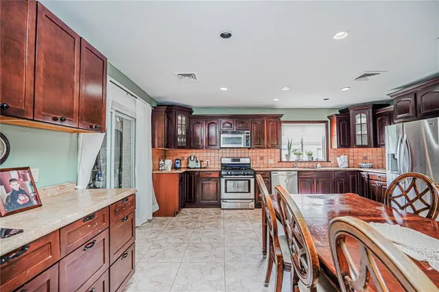 a kitchen with stainless steel appliances kitchen island granite countertop a table chairs and a refrigerator