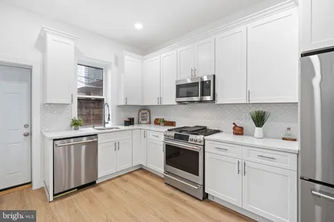 a kitchen with stainless steel appliances granite countertop white cabinets a sink a stove a refrigerator and microwave with wooden floor