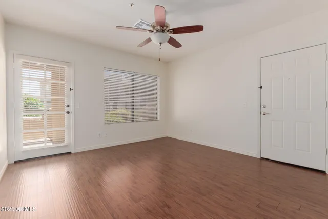 an empty room with wooden floor chandelier fan and windows