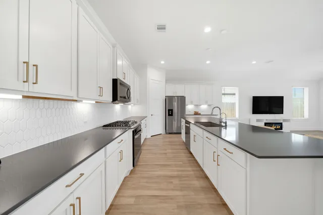 a large kitchen with stainless steel appliances granite countertop a sink dishwasher a stove and a oven with wooden floor