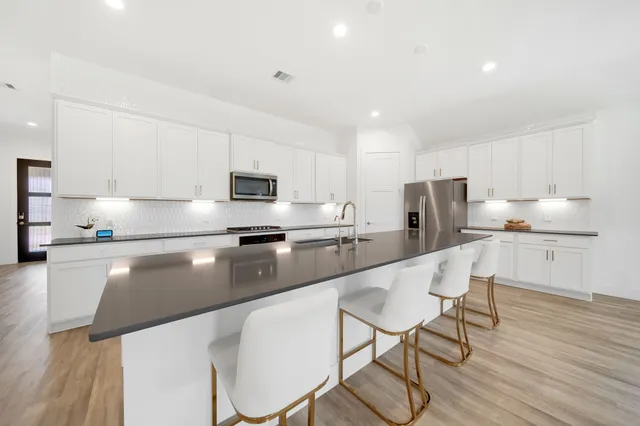 a modern kitchen with stainless steel appliances granite countertop a stove a sink a refrigerator with a dining table and chairs