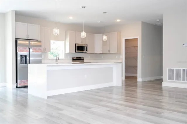 a large white kitchen with kitchen island a sink stainless steel appliances and cabinets