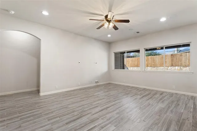 an empty room with wooden floor fan and windows